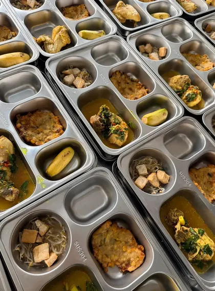 Deretan tray stainless yang sedang diisi tahu dengan tauge, bakwan jagung, dan lauk berkuah.