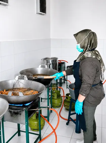 Staf memasak menggunakan wajan besar di dapur produksi.