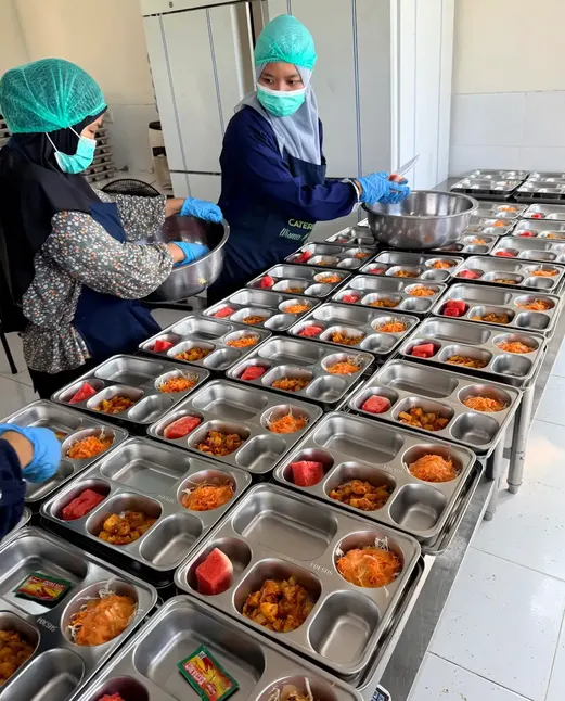 Staf mengisi deretan tray makanan yang siap dikemas.