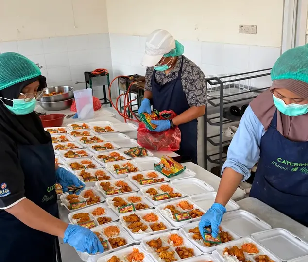 Tim menyiapkan kotak makan sekali pakai di meja penyiapan panjang.