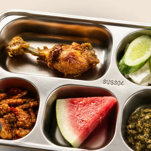 Nampan stainless paket personal berisi ayam goreng, sambal, semangka, dan irisan timun.